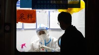 Seorang pekerja dengan pakaian pelindung menunggu untuk memberikan tes COVID-19 di tempat pengujian virus corona di Beijing.