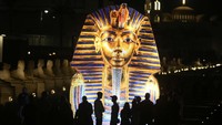 Turis berdiri di depan spanduk raksasa yang menunjukkan topeng emas Raja Tutankhamun di kuil Luxor di Luxor, Mesir, Jumat, 4 November 2022.
