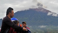 Pengendara melintas saat Gunung Kerinci mengembuskan gas dan material ke udara yang terlihat dari Kayu Aro, Kerinci, Jambi, Sabtu (5/11/2022). 