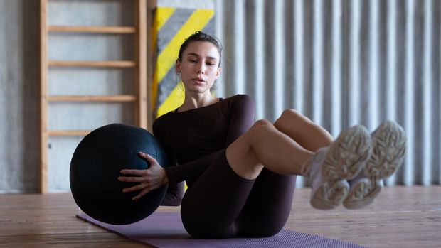 Woman doing russian twists with a medicine ball.