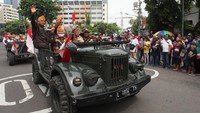 Konvoi Mobil Jeep yang ditumpangi oleh warga dengan menggunakan pakaian pahlawan pada jaman perang.