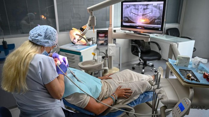 A dentist and his assistant work on a patient at a dental clinic in Istanbul on September 16, 2022. - Attracted by unbeatable prices, fast turnaround times and the promise of a bright smile, 150,000 to 250,000 foreign patients will travel to Turkey for treatment this year, according to the Turkish Dental Association (TDB), making the country one of the main destinations of world dental tourism. (Photo by Ozan KOSE / AFP) (Photo by OZAN KOSE/AFP via Getty Images)