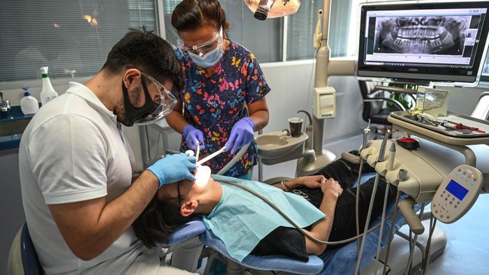 A dentist and his assistant work on a patient at a dental clinic in Istanbul on September 16, 2022. - Attracted by unbeatable prices, fast turnaround times and the promise of a bright smile, 150,000 to 250,000 foreign patients will travel to Turkey for treatment this year, according to the Turkish Dental Association (TDB), making the country one of the main destinations of world dental tourism. (Photo by Ozan KOSE / AFP) (Photo by OZAN KOSE/AFP via Getty Images)