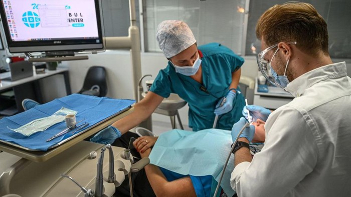Ramai Wisata Dokter Gigi di Turki, Pasien dari Luar Negeri Lho A dentist and his assistant work on a patient at a dental clinic in Istanbul on September 16, 2022. - Attracted by unbeatable prices, fast turnaround times and the promise of a bright smile, 150,000 to 250,000 foreign patients will travel to Turkey for treatment this year, according to the Turkish Dental Association (TDB), making the country one of the main destinations of world dental tourism. (Photo by Ozan KOSE / AFP) (Photo by OZAN KOSE/AFP via Getty Images)