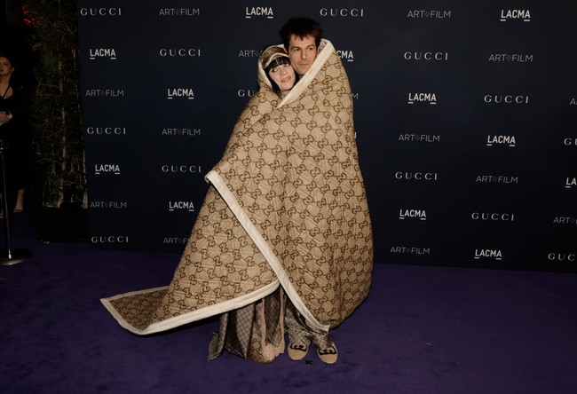 Selimut Gucci ukuran besar membungkus Billie Eilish dan Jesse Rutherford yang saling berpelukan saat berpose di depan para juru foto. Foto: FilmMagic/Steve Granitz via Getty Images