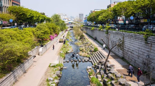 Orang-orang menggunakan batu loncatan untuk berjalan melintasi sungai Cheonggyecheon di Seoul pada 18 April 2022. ANTHONY WALLACE/AFP via Getty Images)