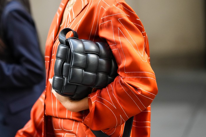 NEW YORK, NEW YORK - SEPTEMBER 13: A guest wears an orange with embroidered white print pattern oversized silk shirt, a black shiny leather puffy Cassette handbag from Bottega Veneta , outside Brandon Maxwell, during New York Fashion Week, on September 13, 2022 in New York City. (Photo by Edward Berthelot/Getty Images)