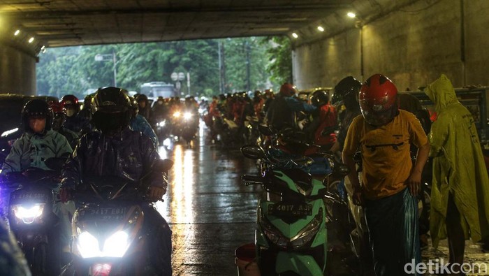 Sejumlah pemotor berteduh di kolong Tol jalan DI Panjaitan, Jakarta Timur, saat hujan turun. Akibatnya lalu lintas tersendat.