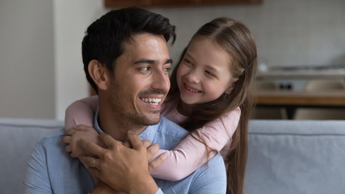 Caring dad enjoy warm moments of tenderness with little daughter. Preschool girl piggyback loving daddy sit together on sofa spend leisure at home. Family ties, happy fathers day celebration concept