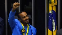 Hamilton yang tersenyum, mengenakan setelan biru kerajaan, menerima medali penghargaan legislatif Brazil, diploma, dan berpidato berterima kasih kepada para penggemarnya dan mendedikasikan kehormatan itu untuk Senna.