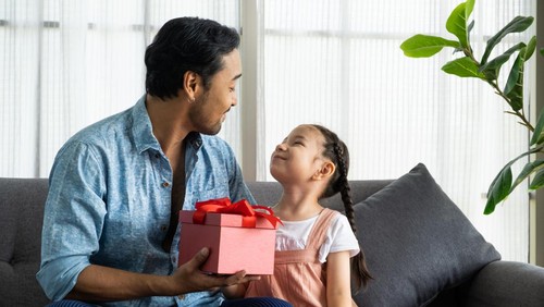 Child Asian girl give a present to his dad while smile, hug and kiss inside of the living room. Happy moment with male parent, family relationship. Father day
