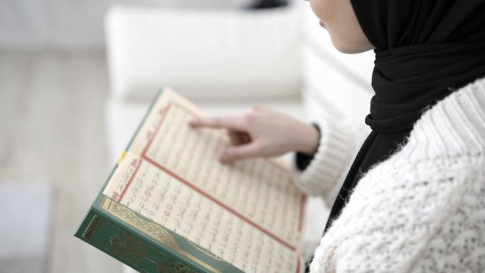 Muslim young woman reading Koran. Horizontal composition.