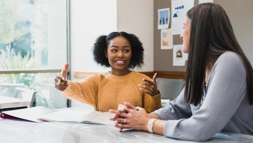 The teenage girl gestures as she explains something to her mid adult female teacher.
