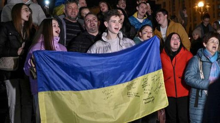 People hold a Ukranian flag as they gather in Maidan square to celebrate the liberation of Kherson, in Kyiv on November 11, 2022, amid the Russian invasion of Ukraine. - Ukraines President Volodymyr Zelensky said on November 11 that Kherson was 