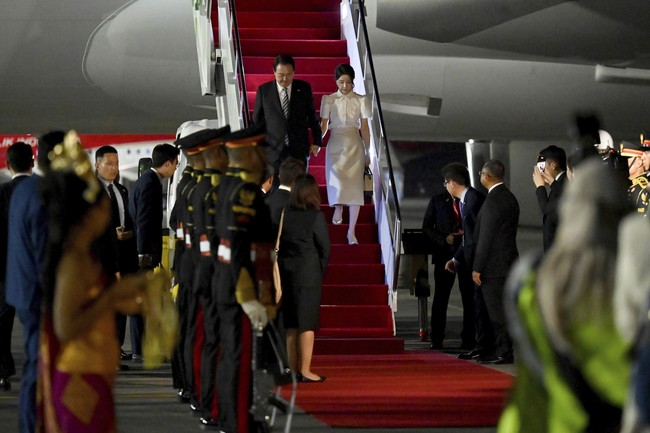 Presiden Korea Selatan Yoon Suk Yeo dan istri, Kim Keon Hee, mendarat di Bali pada Minggu (13/11/2022) malam. Keluar dari pesawat kepresidenan, keduanya terlihat rapi dalam balutan busana formal. Kim Keon Hee memakai setelan berjas gelap, sementara Kim Keon Hee memilih blus dan rok berpalet muted.    (Foto: Sonny Tumbelaka/Pool Photo via AP)