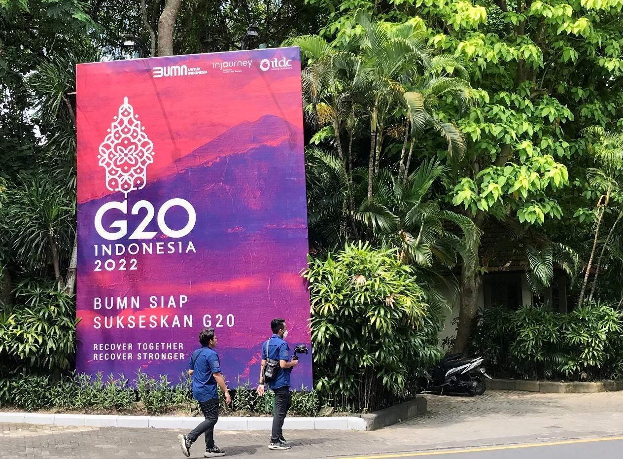 Orang-orang berjalan melewati spanduk berlogo G20 di Bali