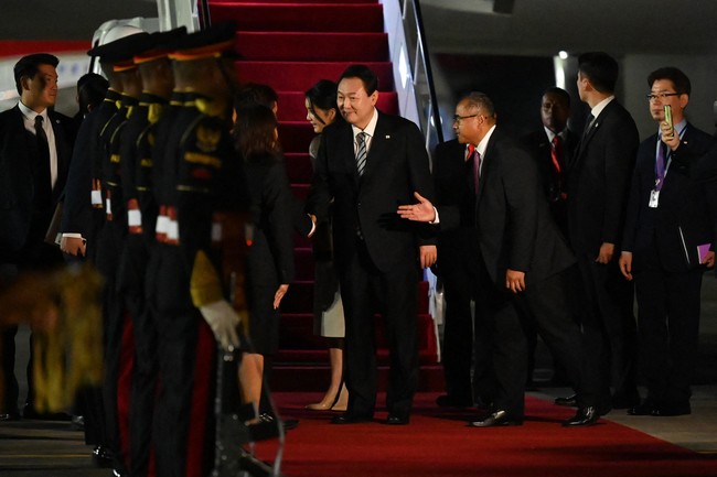 Menjadi tuan rumah KTT G20 2022 pada 15-16 November 2022, Bali kedatangan para pemimpin dunia. Salah satunya Presiden Korea Selatan Yoon Suk Yeol yang tiba di Bandara Internasional I Gusti Ngurah-Rai pada Minggu (13/11/2022). Didampingi Ibu Negara Kim Keon Hee, pria 61 tahun tampil formal dalam balutan setelan hitam berjas lengkap dengan dasi abu-abu bermotif garis hitam. (Foto: POOL/AFP via Getty Images/SONNY TUMBELAKA)