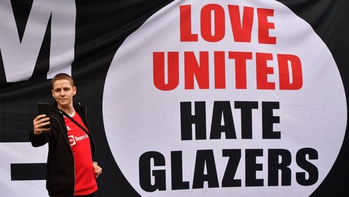 A supporter takes a photograph beside anti-Glazer banners, as protesters gather outside Old Trafford stadium to demonstrate against Manchester Uniteds owners ahead of the English Premier League football match between Manchester United and Liverpool at Old Trafford in Manchester, north west England, on August 22, 2022. - The large-scale protest by United fans before kick-off is aimed at the clubs owners, the Glazer family. (Photo by ANTHONY DEVLIN / AFP) (Photo by ANTHONY DEVLIN/AFP via Getty Images)