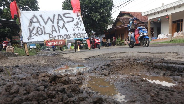 Pengendara sepeda motor melintas di jalan rusak yang dipasang banner di jalan utama Kediri-Tulungagung, Desa Mondo, Kediri, Jawa Timur, Rabu (16/11/2022). Warga daerah setempat memberi tanda pada lubang jalan dengan banner sebagai bentuk protes karena jalan rusak yang tidak kunjung diperbaiki. ANTARA FOTO/Prasetia Fauzani/foc.