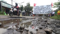 Pengendara sepeda motor melintas di jalan rusak yang dipasang banner di jalan utama Kediri-Tulungagung, Desa Mondo, Kediri, Jawa Timur, Rabu (16/11/2022).