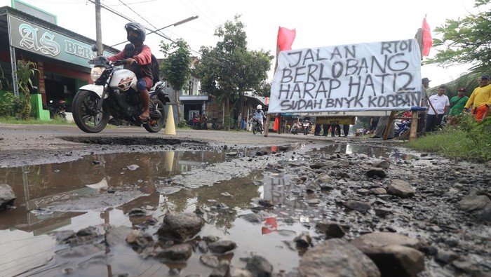 Pengendara sepeda motor melintas di jalan rusak yang dipasang banner di jalan utama Kediri-Tulungagung, Desa Mondo, Kediri, Jawa Timur, Rabu (16/11/2022). Warga daerah setempat memberi tanda pada lubang jalan dengan banner sebagai bentuk protes karena jalan rusak yang tidak kunjung diperbaiki. ANTARA FOTO/Prasetia Fauzani/foc.