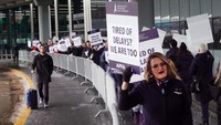 Calon penumpang pesawat melintas di semping aksi karyawan American Airlines.