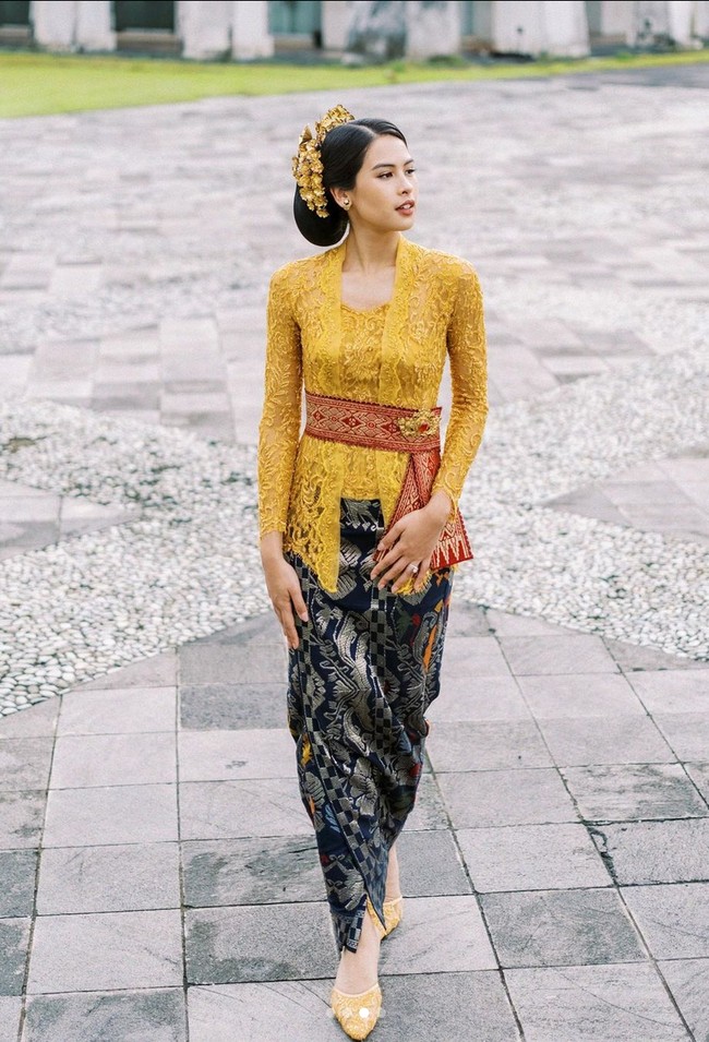 Maudy Ayunda kembali mempercayakan Didiet Maulana untuk merancang busananya. Kebaya warna mustard ini terlihat unik dengan model kerah asimetris. Obi merah dari tenun berbordir emas mengaksentuasi pinggang. Foto: Instagram @maudyayunda