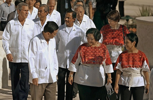 Di APEC 2002 yang berlangsung di Meksiko, para pria memakai guayabera berwarna putih. Seperti kemeja biasa, hanya saja baju ini memiliki kantong yang lebih banyak dan dihiasi detail bordiran. Adapun para wanita, seperti Presiden Megawati Soekarnoputri memakai tunik bermotif etnik yang dipermanis dengans sabuk tali. (Foto: AFP via Getty Images/ROBERTO SCHMIDT)