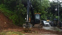 Petugas membersihkan jalanan dengan menggunakan alat berat untuk mengangkat material longsor.
