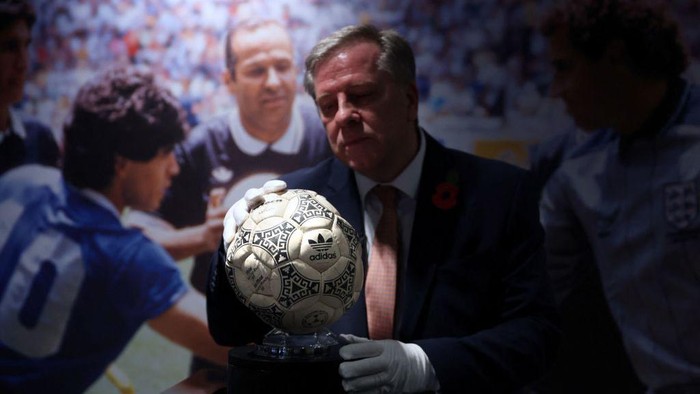Penampakan Bola 'Gol Tangan Tuhan' Maradona yang Bakal Dilelang Graham Budd poses with the match ball used in the 1986 FIFA World Cup Quarter-Final football match between Argentina and England, played at the Estadio Azteca, Mexico City, during a photocall ahead of its auction, at Wembley Stadium in London on November 1, 2022. - The ball that Diego Maradona used to score his infamous
