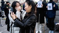 Seorang siswa (kiri) membawa pendukung yang memegang selembar kertas bertuliskan suporter dan suneung, di luar Ehwa Girls Foreign Language High School di Seoul 17 November 2022. Foto: AFP via Getty Images/ANTHONY WALLACE