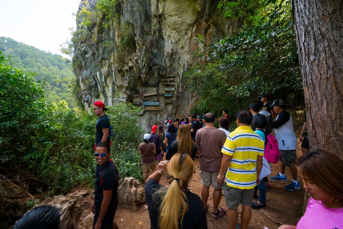 Kuburan gantung di Sagada, Filipina Sagada, Philippines - April 30, 2017: Sagada view showing hanging coffins in the rock mountain, trees and tourists visiting and taking pictures can be seen on the background