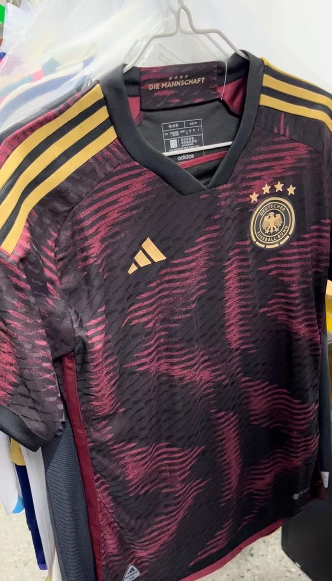 Jersey tandang Jerman terlihat cukup stylish dan unik dengan perpaduan warna hitam dan merah muda keunguan. Bagian pundaknya dihiasi dengan 3 garis berwarna emas. Senada dengan warna garis pada bagian pundaknya, logo Adidas dan sepak bola Jerman di bagian dada juga berwarna keemasan. Foto: Twitter/@Soccerdealshop1