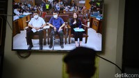 Sebuah layar televisi menyiarkan sidang ini. 