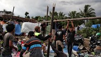 Warga gotong-royong membangun tenda darurat di pinggir sawah. Tenda darurat itu menggunakan rangka bambu dan beratapkan terpal.