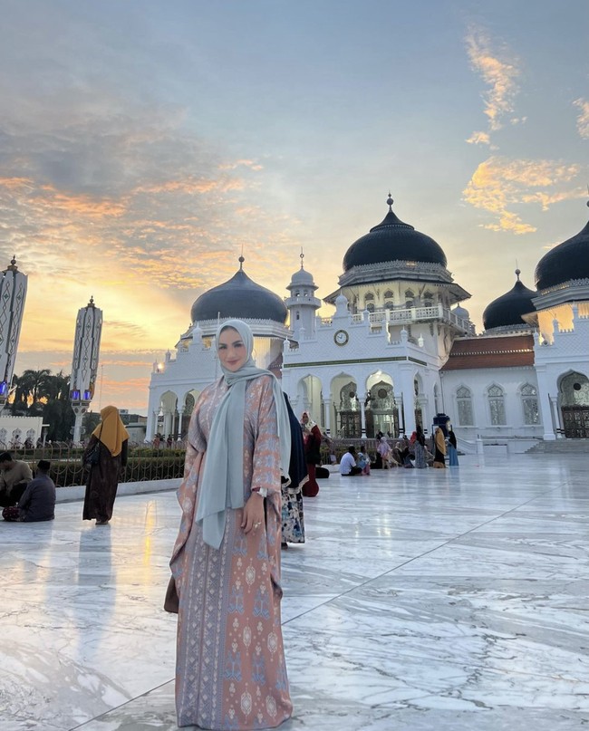 Wanita yang lahir 24 Maret 1975 di Batu, Jawa Timur ini mengunggah foto OOTD menggunakan kaftan panjang bahan satin motif print songket saat berpose di Masjid Raya Baiturrahman, Banda Aceh.  Foto: Dok. Instagram @krisdayantilemos.