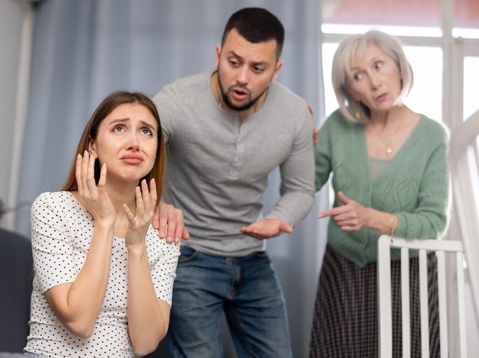 1417984614 Offended woman sitting on sofa in apartment. Her husband and mother-in-law quarreling with her.