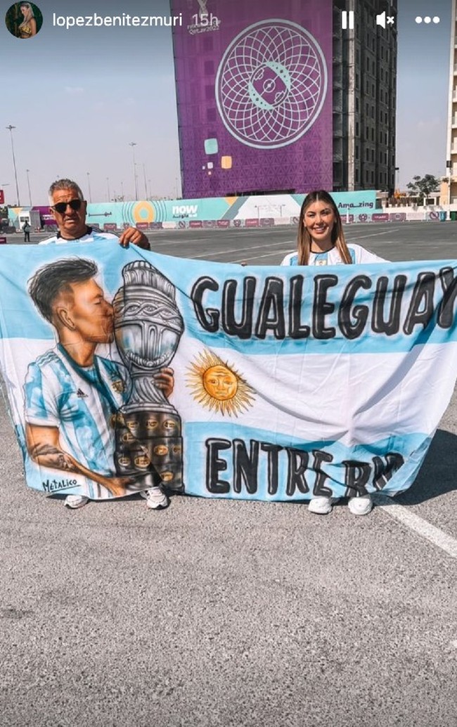Melalui unggahan di Instagram Story, Muri Lopez Benitez memperlihatkan momen dirinya berada di Qatar untuk menonton pertandingan perdana Argentina di Piala Dunia 2022. Dia berpose sambil membentangkan spanduk bergambar wajah kekasihnya, Lisandro Martinez. Foto: Dok. Instagram @lopezbenitezmuri