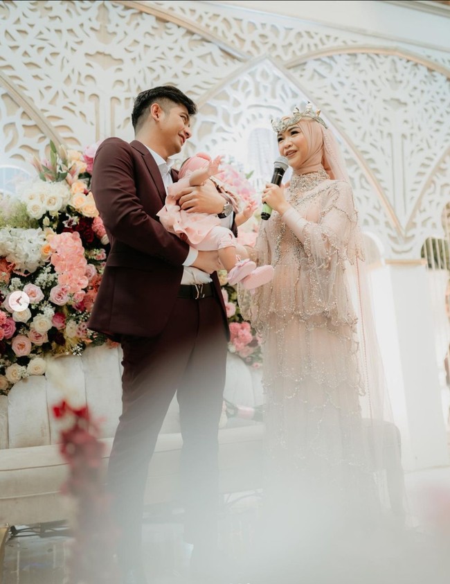 Sementara sang suami, Teuku Ryan tampil gagah mengenakan setelan jas berwarna marun. Kebahagiaan keduanya tentu kini semakin lengkap dengan kehadiran sang buah hati yang turut diajak menghadiri perayaan anniversary Ricis dan Ryan. Foto: Instagram/@studiokencana