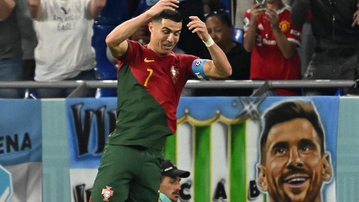 TOPSHOT - Portugals forward #07 Cristiano Ronaldo celebrates after scoring his teams first goal from the penalty spot as a banner depicting Argentine forward Lionel Messi is seen at the back during the Qatar 2022 World Cup Group H football match between Portugal and Ghana at Stadium 974 in Doha on November 24, 2022. (Photo by MANAN VATSYAYANA / AFP) (Photo by MANAN VATSYAYANA/AFP via Getty Images)