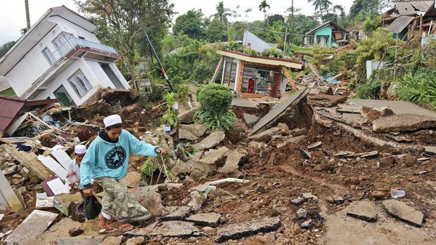 Seorang anak dalam kondisi luka dievakuasi ayahnya menuju pengungsian di Cianjur. Anak itu dievakuasi dengan cara digendong melintasi puing-puing bangunan.