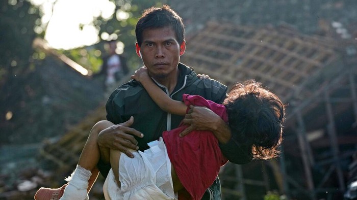 Seorang anak dalam kondisi luka dievakuasi ayahnya menuju pengungsian di Cianjur. Anak itu dievakuasi dengan cara digendong melintasi puing-puing bangunan.