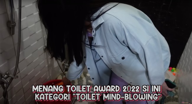 Di sebelah kloset duduk tersebut terdapat sebuah ember merah dengan gayung berwarna oranye. Ini rumahnya benar-benar tetap kearifan lokal ya. Toilet hadap-hadapan, jongkok, sama duduk, sama ember, ada gayung oranye. Ini gayung yang sering gue cela-cela nih, terang Hesti sambil bercanda. Foto: YouTube/Hesti Purwadinata