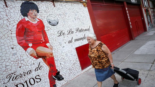 Seorang wanita berjalan melewati mural yang dibuat dengan ubin yang menggambarkan legenda sepak bola Argentina Diego Armando Maradona. 