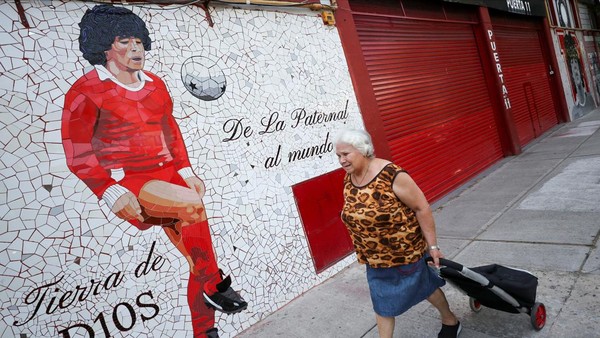 Seorang wanita berjalan melewati mural yang dibuat dengan ubin yang menggambarkan legenda sepak bola Argentina Diego Armando Maradona. Seorang wanita berjalan melewati mural yang dibuat dengan ubin yang menggambarkan legenda sepak bola Argentina Diego Armando Maradona.Â