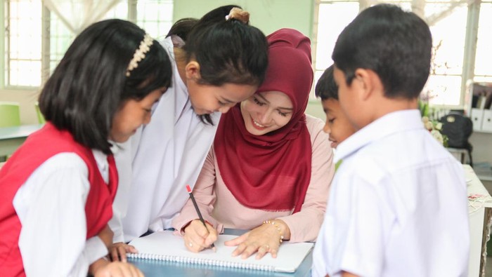 A Malay Muslim female teacher teaching a group of students in a classroom in Malaysia.