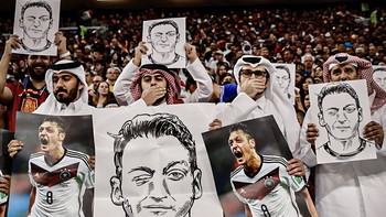 Para fans Qatar mengkritik Jerman dengan poster Mesut Oezil. Oezil pernah mengkritik Jerman terkait rasisme. Foto: (Twitter)