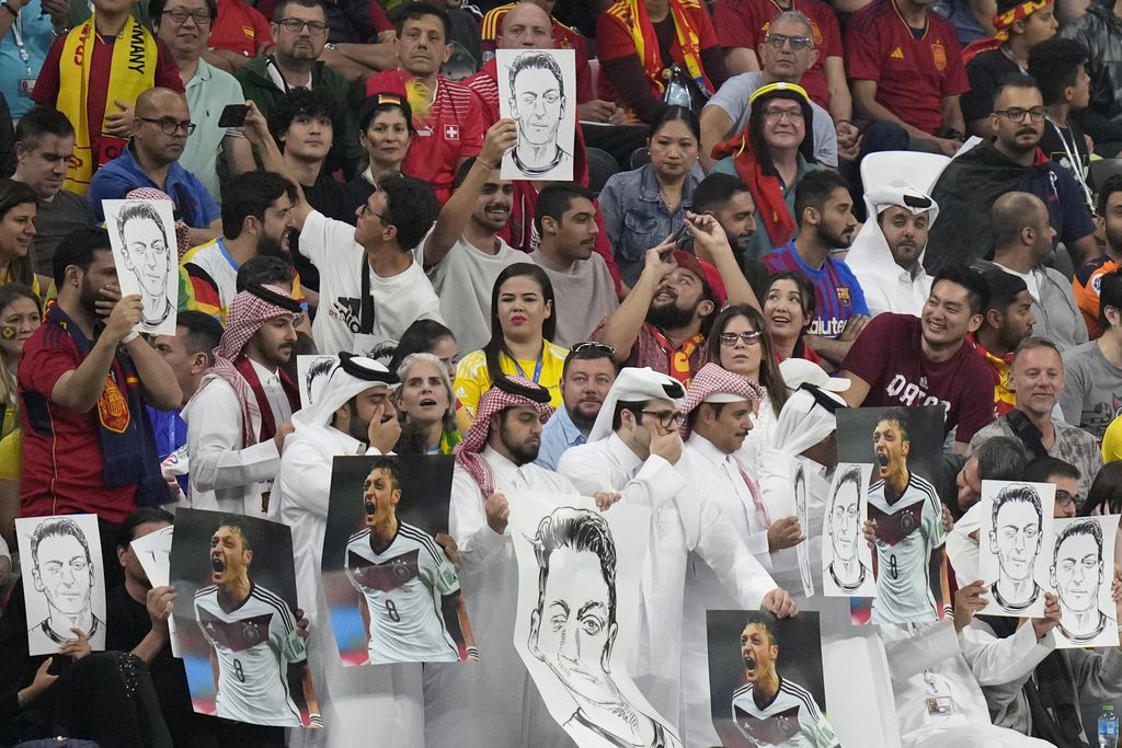 Penonton memegang foto pemain internasional Jerman Forman Mesut Ozil di tribun dan menutup mulut mereka selama pertandingan sepak bola grup E Piala Dunia antara Spanyol dan Jerman, di Stadion Al Bayt di Al Khor, Qatar, Minggu, 27 November 2022. (AP Foto/Matthias Schrader)