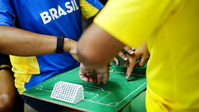 Helio Fonseca, right, helps his deaf and blind friend Carlos Junior, center, with a play-by-play of the World Cup group G soccer match between Brazil and Switzerland, in Osasco, Sao Paulo state, Brazil, Monday, Nov. 28, 2022. Fonseca uses a tactile table and touch on the body of visually and hearing-impaired people to show them the movements of the ball and of the players during soccer matches. Brazil won the match 1-0. (AP Photo/Marcelo Chello)
