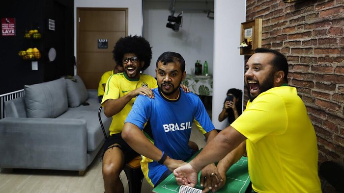 Helio Fonseca, right, helps his deaf and blind friend Carlos Junior, center, with a play-by-play of the World Cup group G soccer match between Brazil and Switzerland, in Osasco, Sao Paulo state, Brazil, Monday, Nov. 28, 2022. Fonseca uses a tactile table and touch on the body of visually and hearing-impaired people to show them the movements of the ball and of the players during soccer matches. Brazil won the match 1-0. (AP Photo/Marcelo Chello)